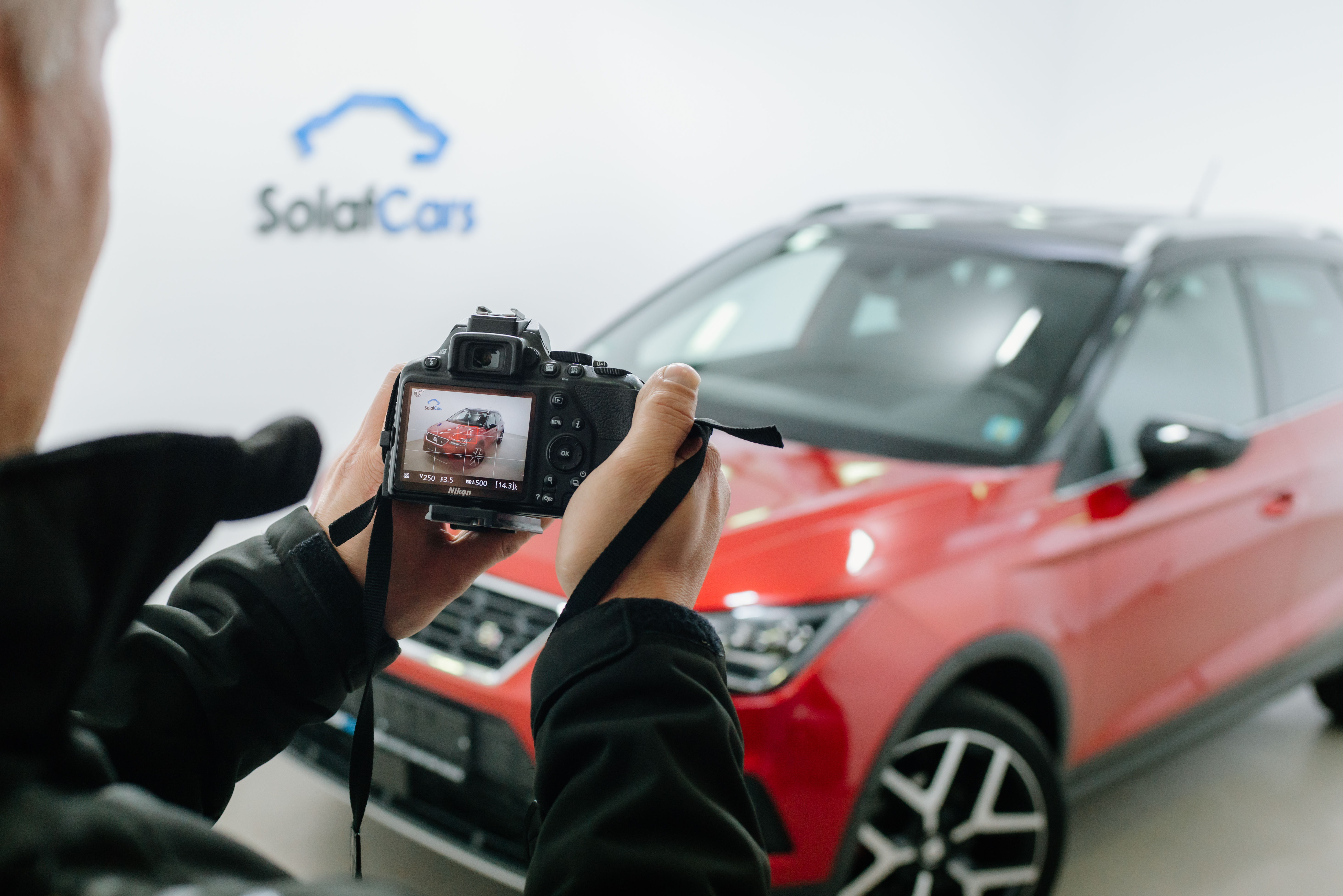 Close-up de um homem tirando uma foto em uma câmera dslr de um carro vermelho em um estúdio de fotografia